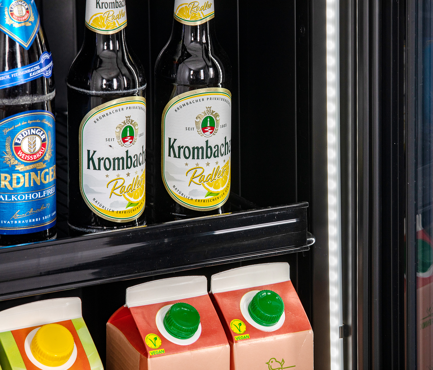 KBS Glastürkühlschrank 327 G Slim, Nahaufnahme von Krombacher Radler Bierflaschen und Saftkartons in der unteren Regalebene.