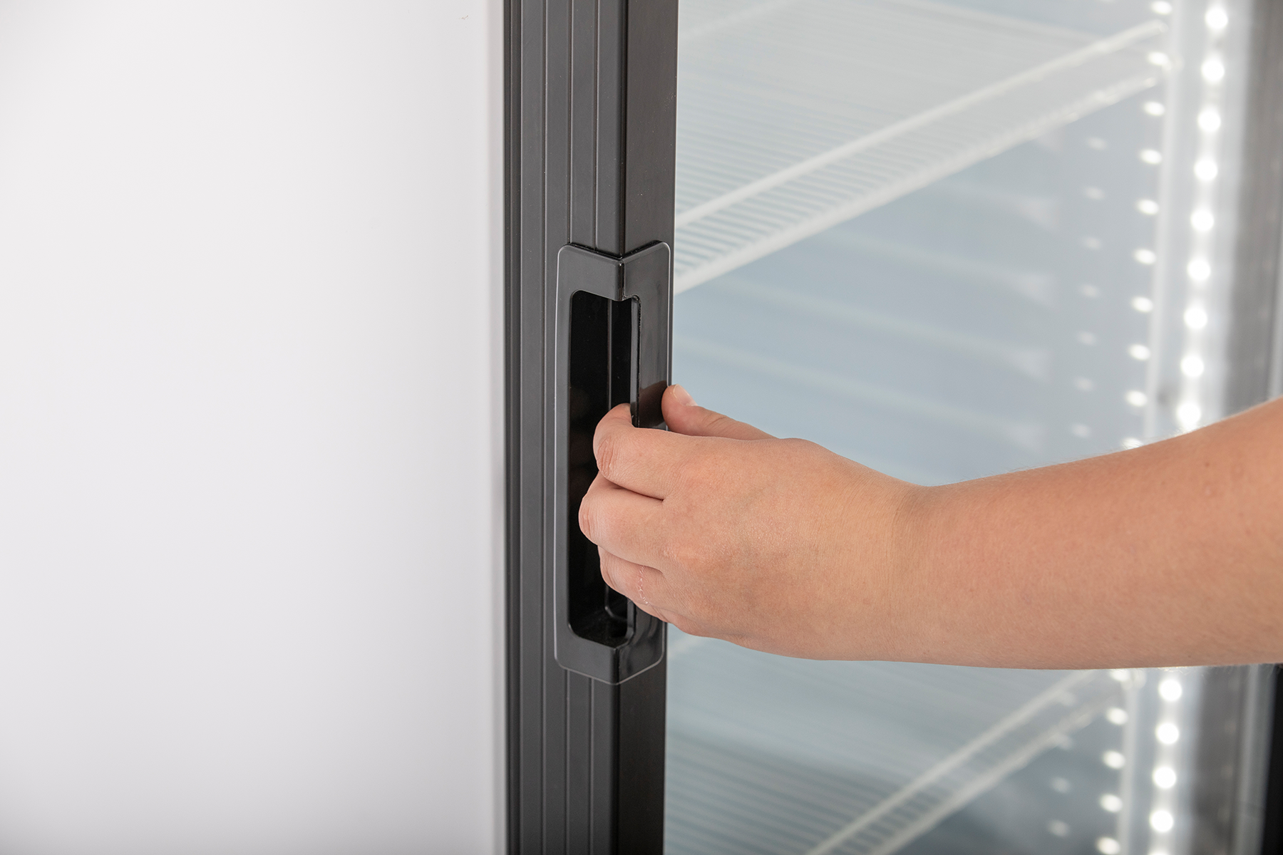 Detailansicht KBS Glastürkühlschrank 375 GDU Nahaufnahme einer Hand, die den schwarzen Türgriff der Glastür betätigt, vor leerem Innenraum mit Regalböden.