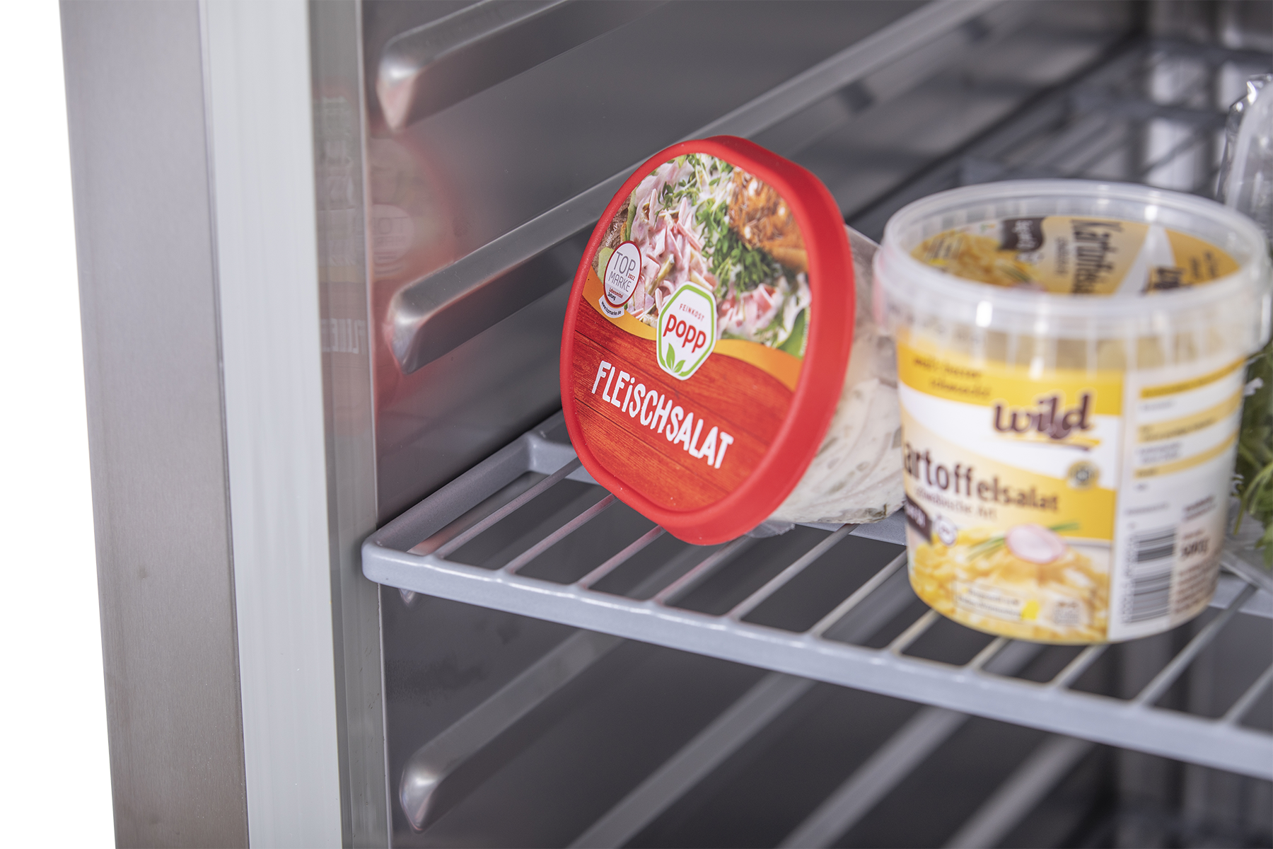 KBS Edelstahlkühlschrank KU 740 Nahaufnahme von Lebensmitteln auf einem Gitterrost, darunter Fleischsalat und Kartoffelsalat, gelagert im Kühlbereich.