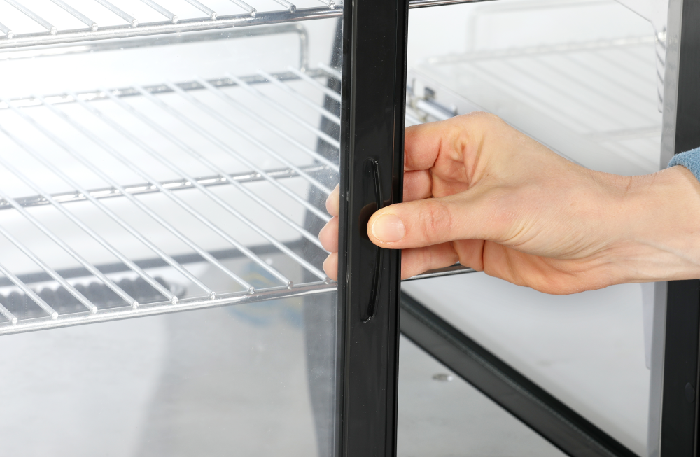 KBS Kühlvitrine, Detailaufnahme einer Hand, die eine Glastür am schwarzen Griff öffnet. Fokus auf ergonomische Bedienbarkeit im Thekenbetrieb, z. B. Bäckerei oder Café.