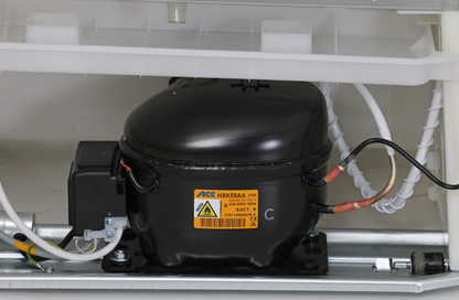 KBS Volltürkühlschrank K311, Nahaufnahme des schwarzen Kompressors mit gelbem Warnetikett, technische Komponente im unteren Bereich des Geräts.